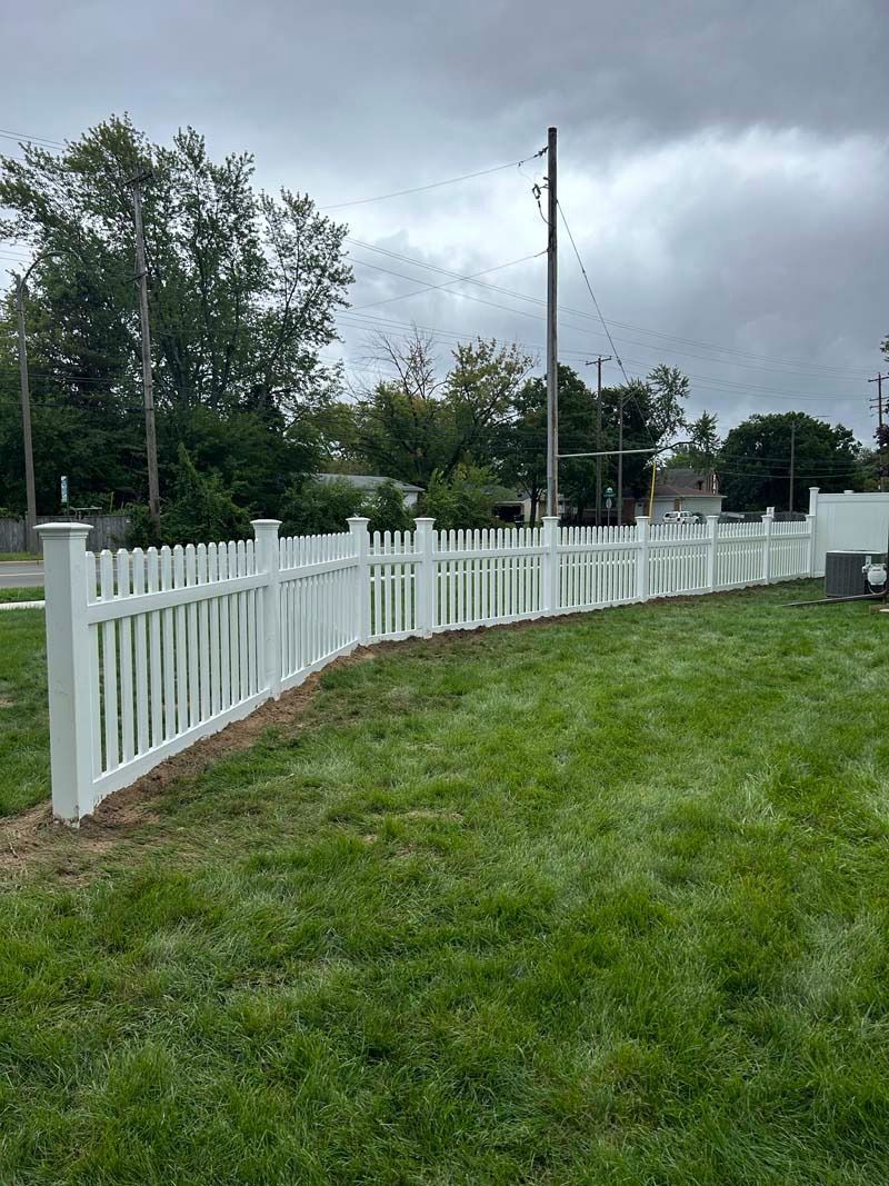 White picket fence curving across a grassy yard under a cloudy sky.