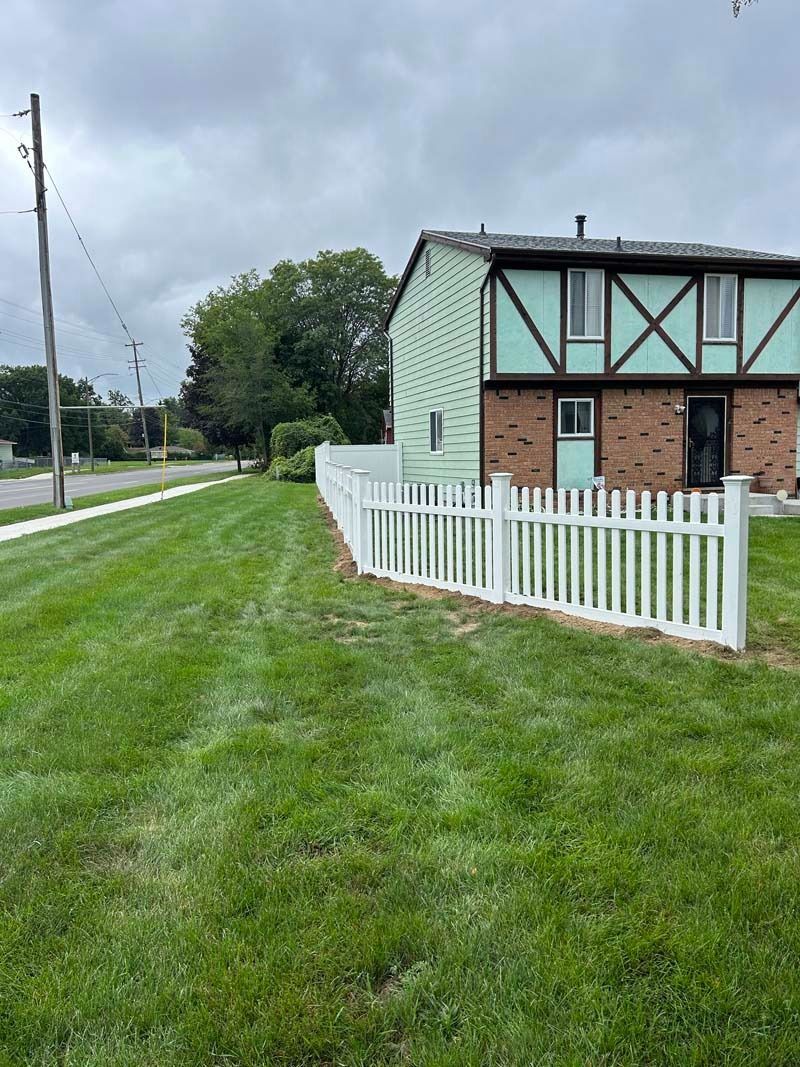 White picket fence bordering a grassy lawn in front of a two-story building with green siding and brown trim.