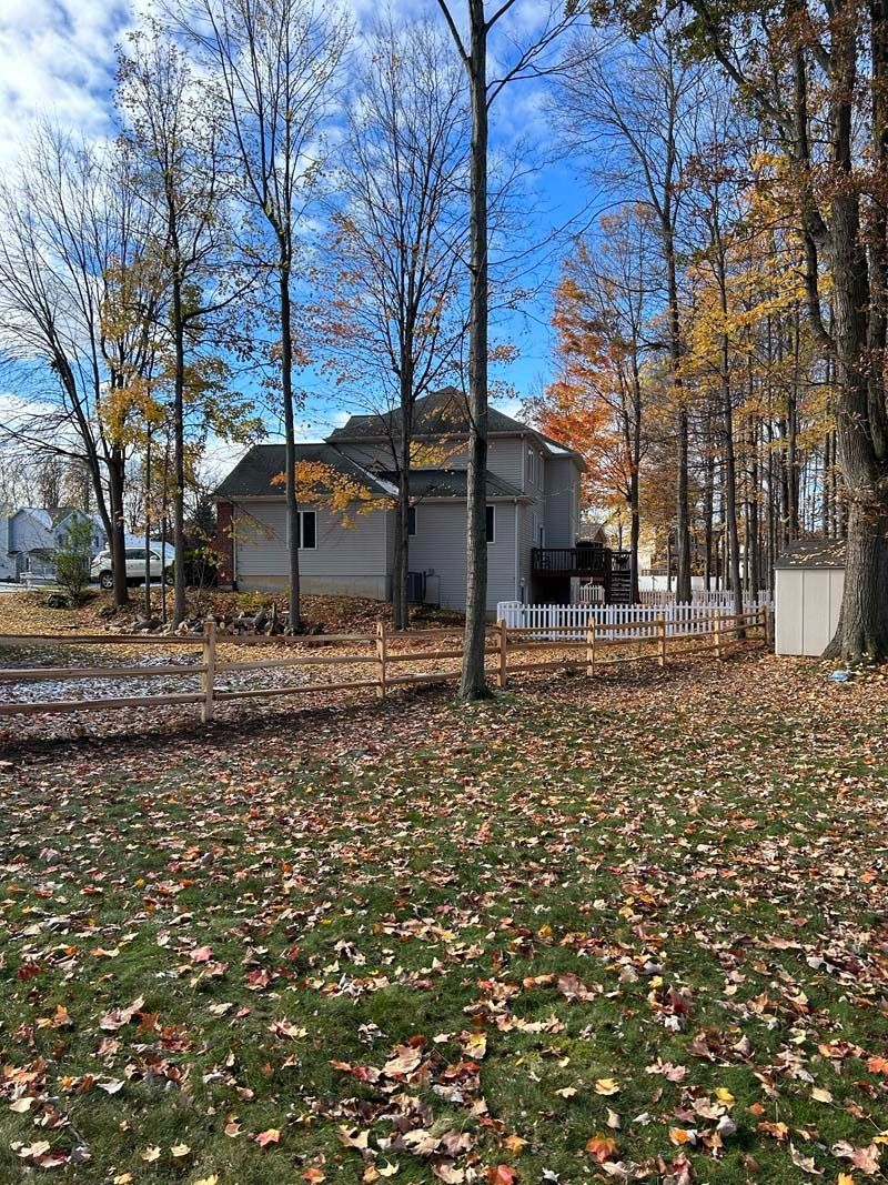 Backyard view of a house with fall foliage and a white picket fence on a sunny day.