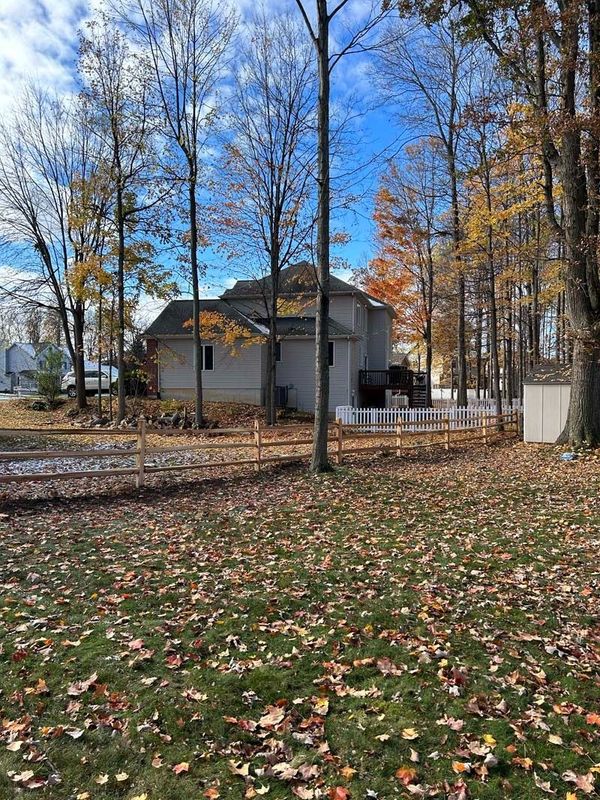 Autumn scene: a house with a yard full of fallen leaves, surrounded by trees with colorful foliage and a bright blue sky.