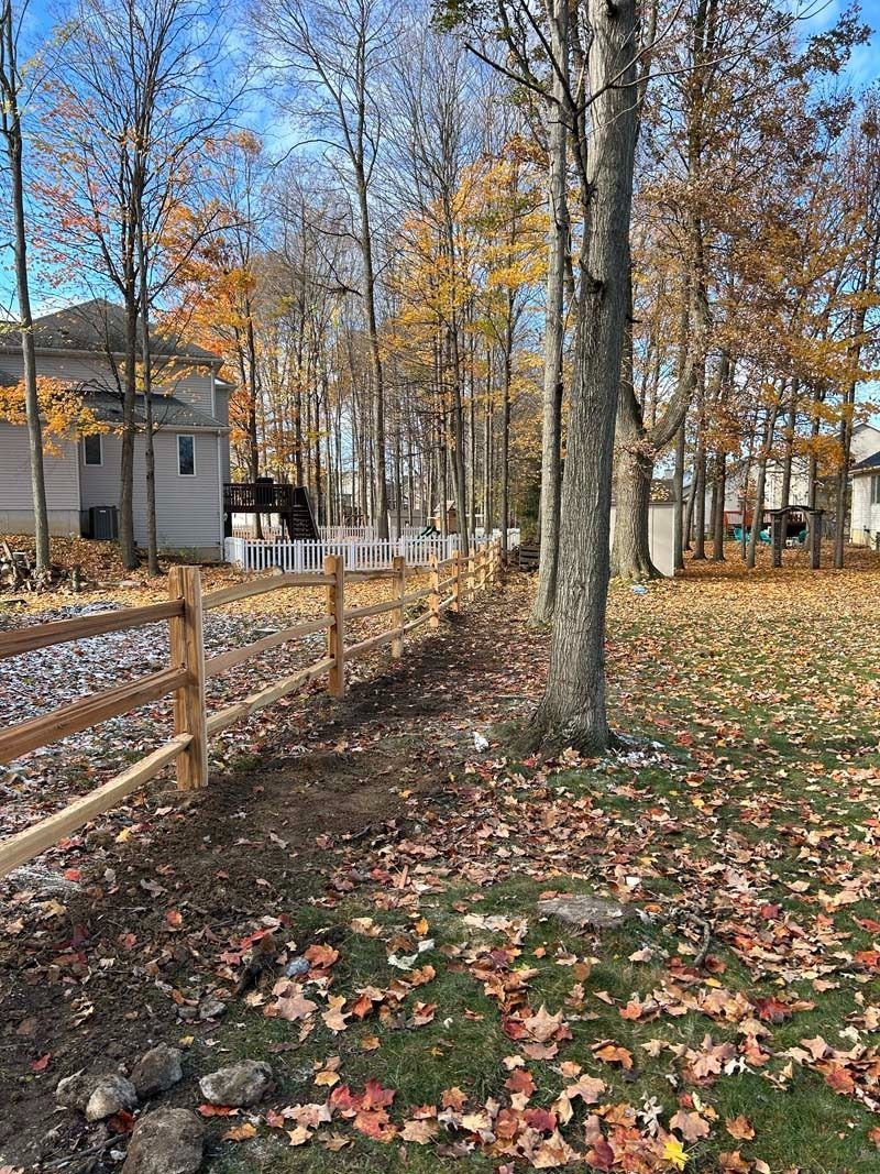 Wooden fence bordering a yard with fallen autumn leaves, trees, and houses in the background.