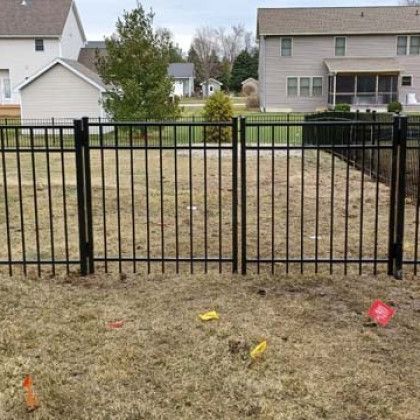 Black metal fence in a yard, with houses in the background and flags on the ground.