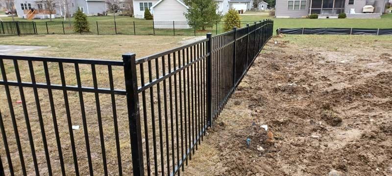 Black metal fence in a yard, with houses in the background.