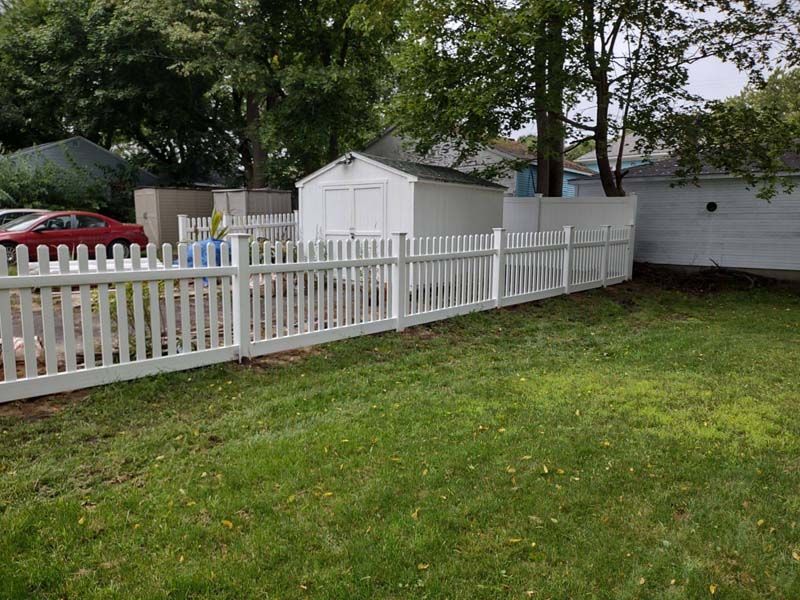 White picket fence enclosing a green backyard with shed, grass, and trees.