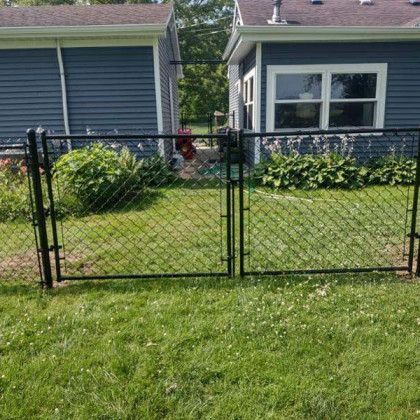 Black chain-link fence with double gate in front of a blue house with a green lawn.