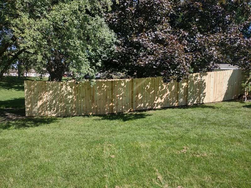 Wooden fence along a grassy lawn, shaded by trees on a sunny day.