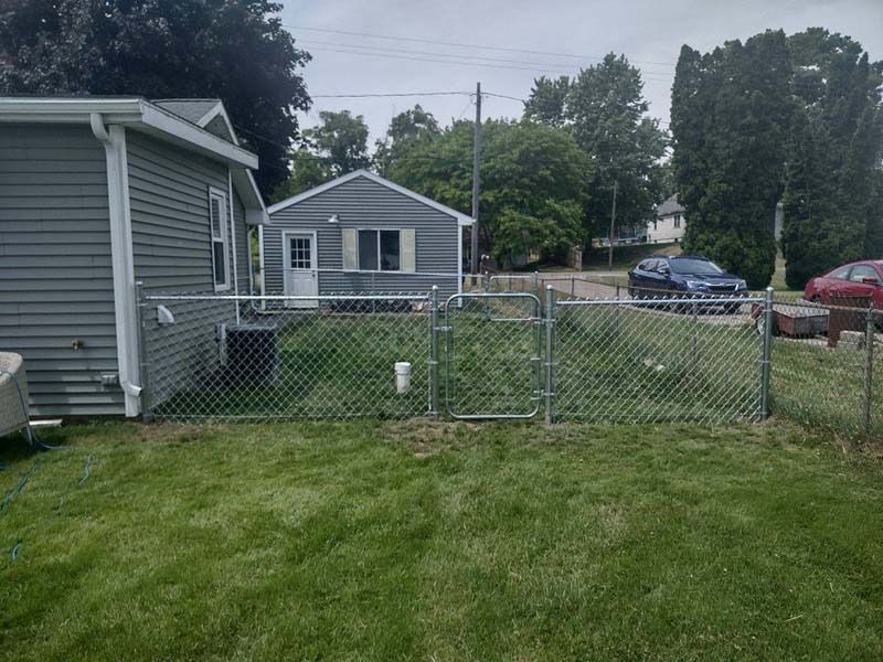 Chain-link fence encloses a grassy yard, with a small house in the background.