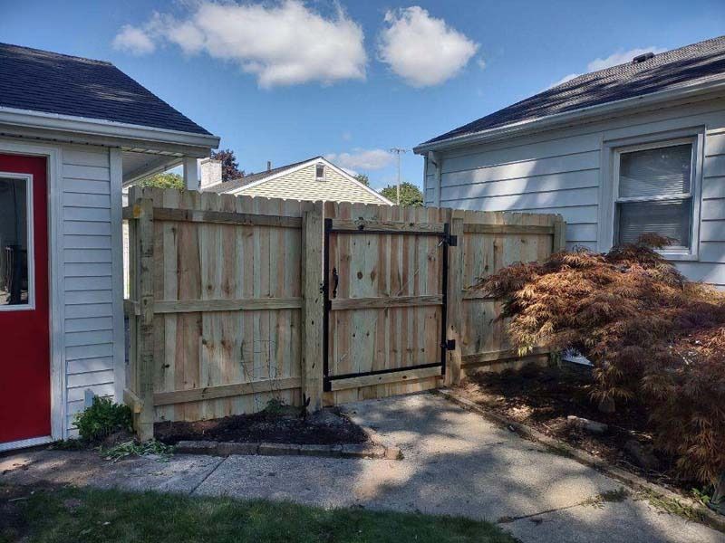 Wooden fence with gate between two houses on a sunny day.