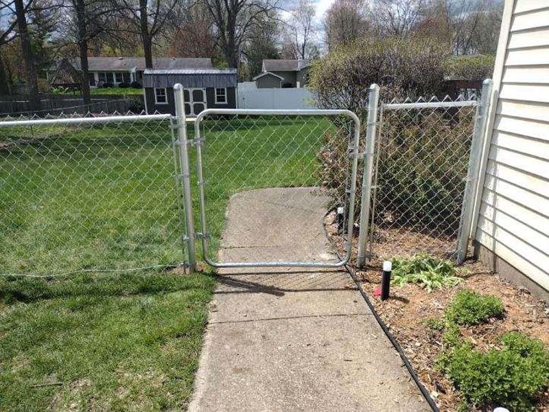 Chain link fence with a gate along a concrete path, leading to a backyard.