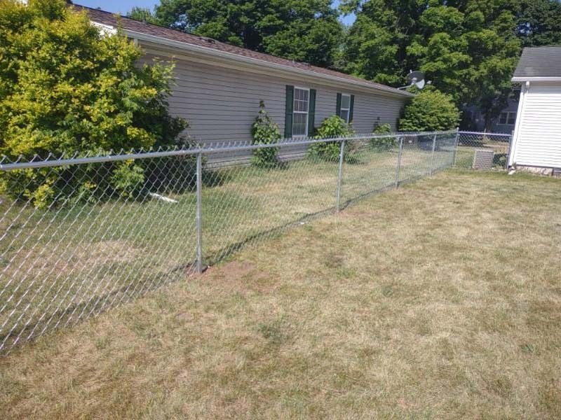 Chain-link fence surrounding a grassy yard, next to a light-colored house.
