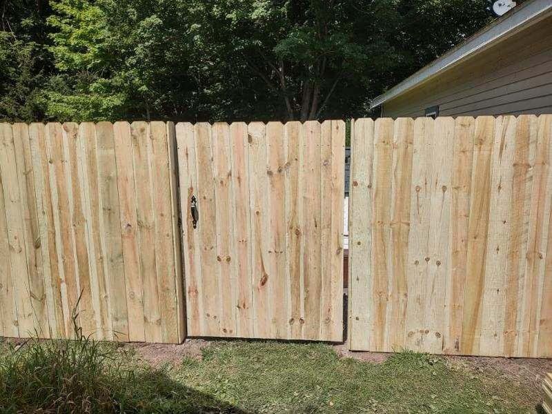 Wooden fence with a gate in a grassy yard next to a house.