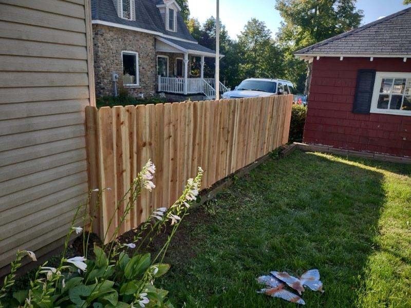 Wooden fence between a tan-sided house and a red-sided house, on a grassy lawn.