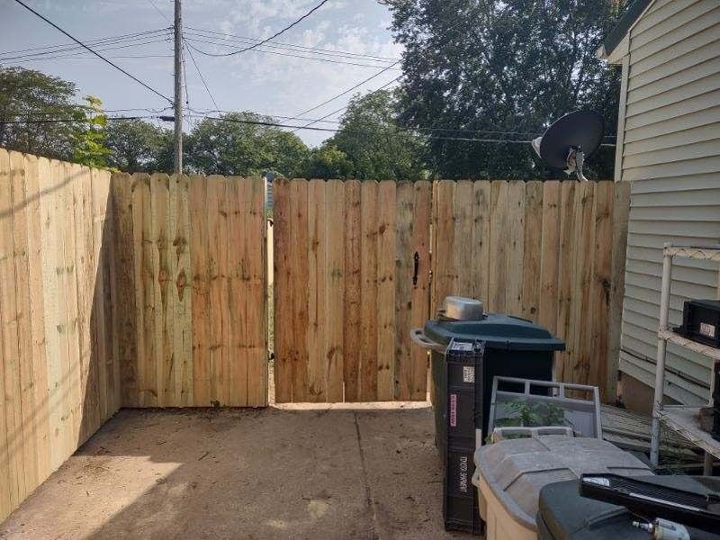 Wooden fence with gate in a backyard, containing trash cans and sunlight.