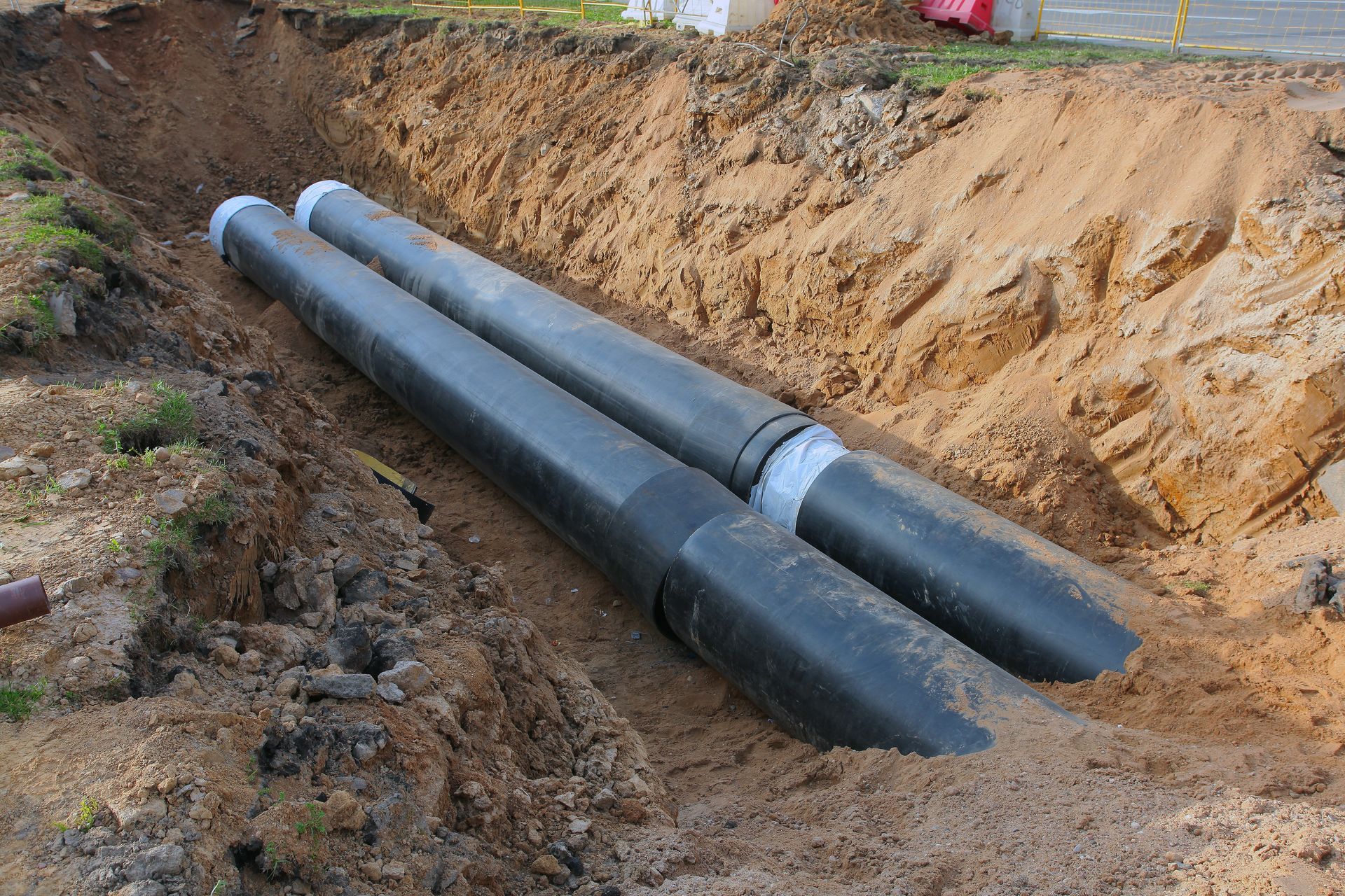 Large black water pipes laid in a deep trench during an underground line replacement.