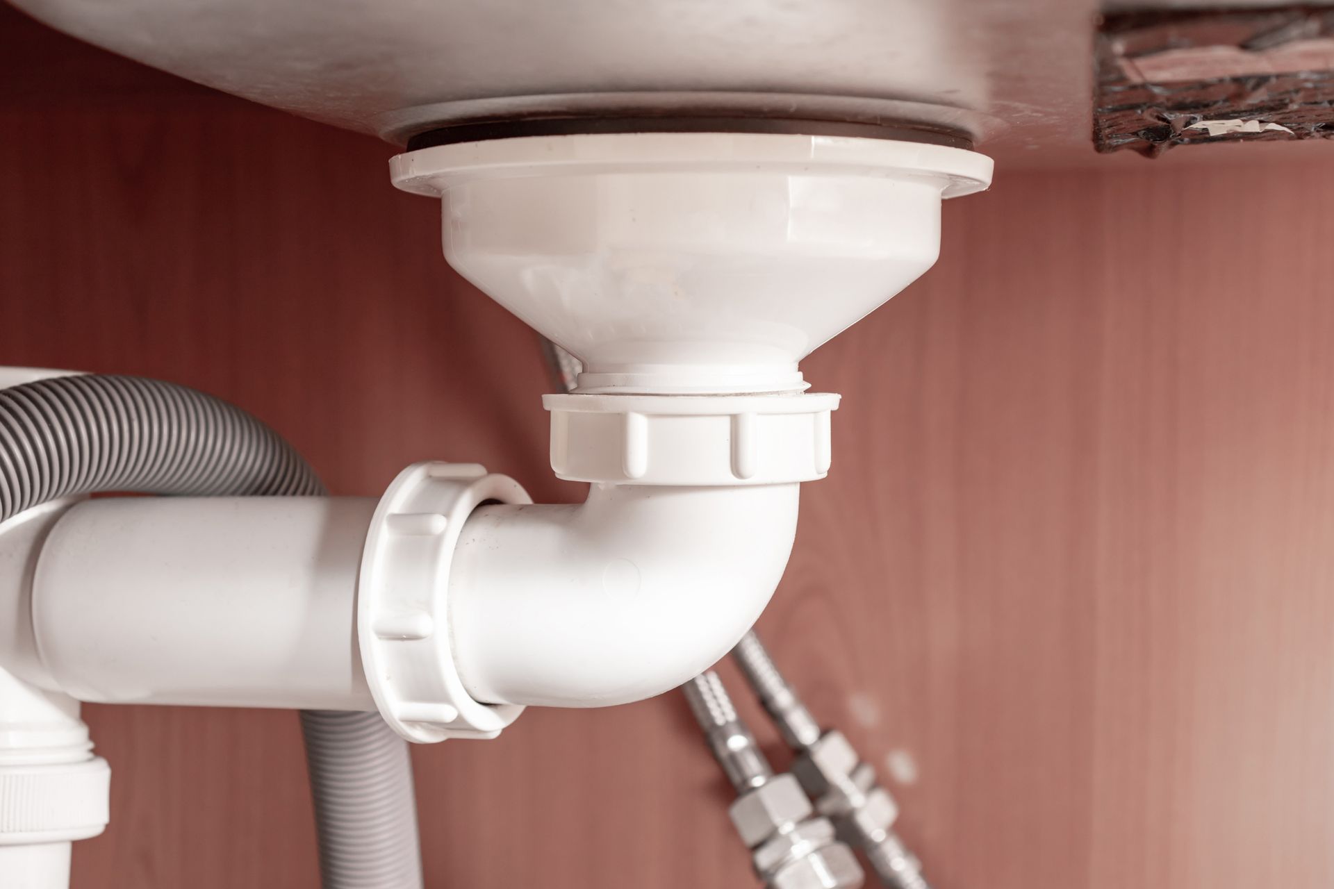 Close-up of hydraulic white PVC pipe under a kitchen sink.