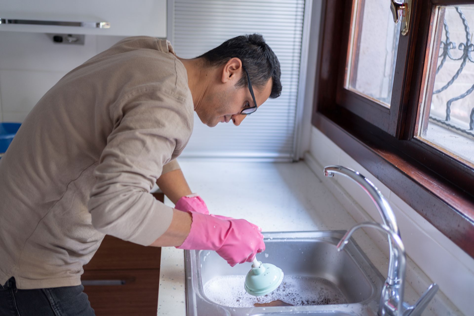 A man using a plunger on a blocked kitchen sink to unclog the drain.