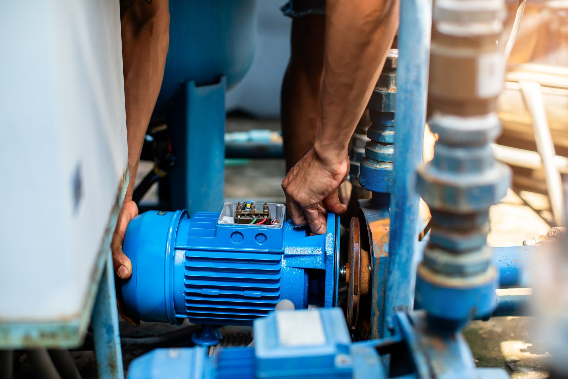 Person working on a blue water pump in an outdoor setting.