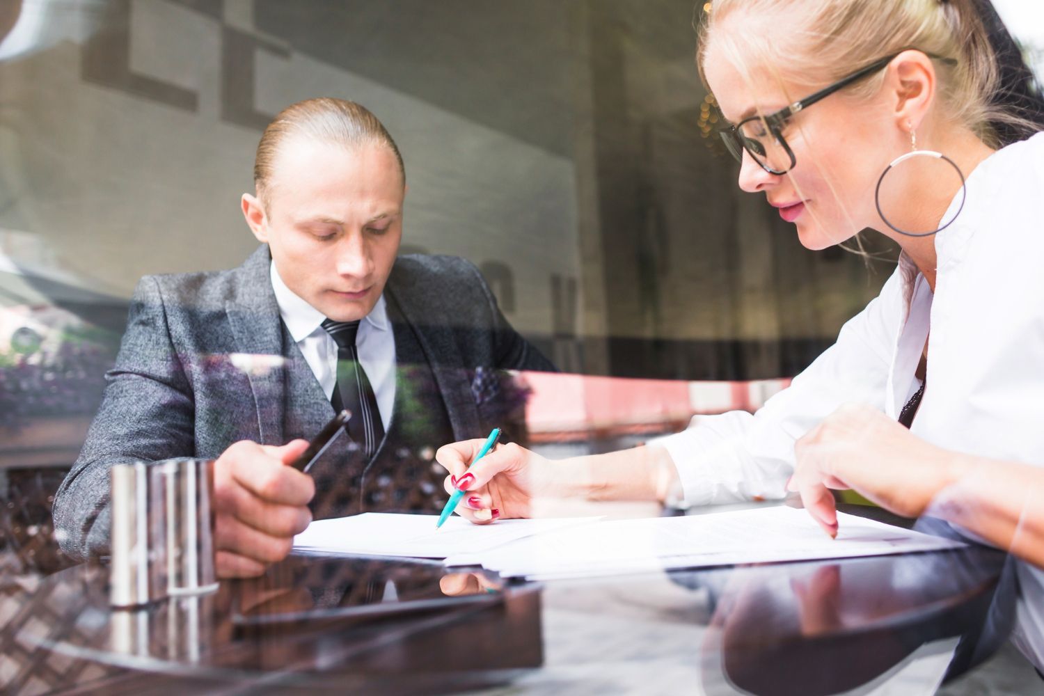 Man and woman in a meeting, reviewing documents at a table. Woman writing, man holding a pen.