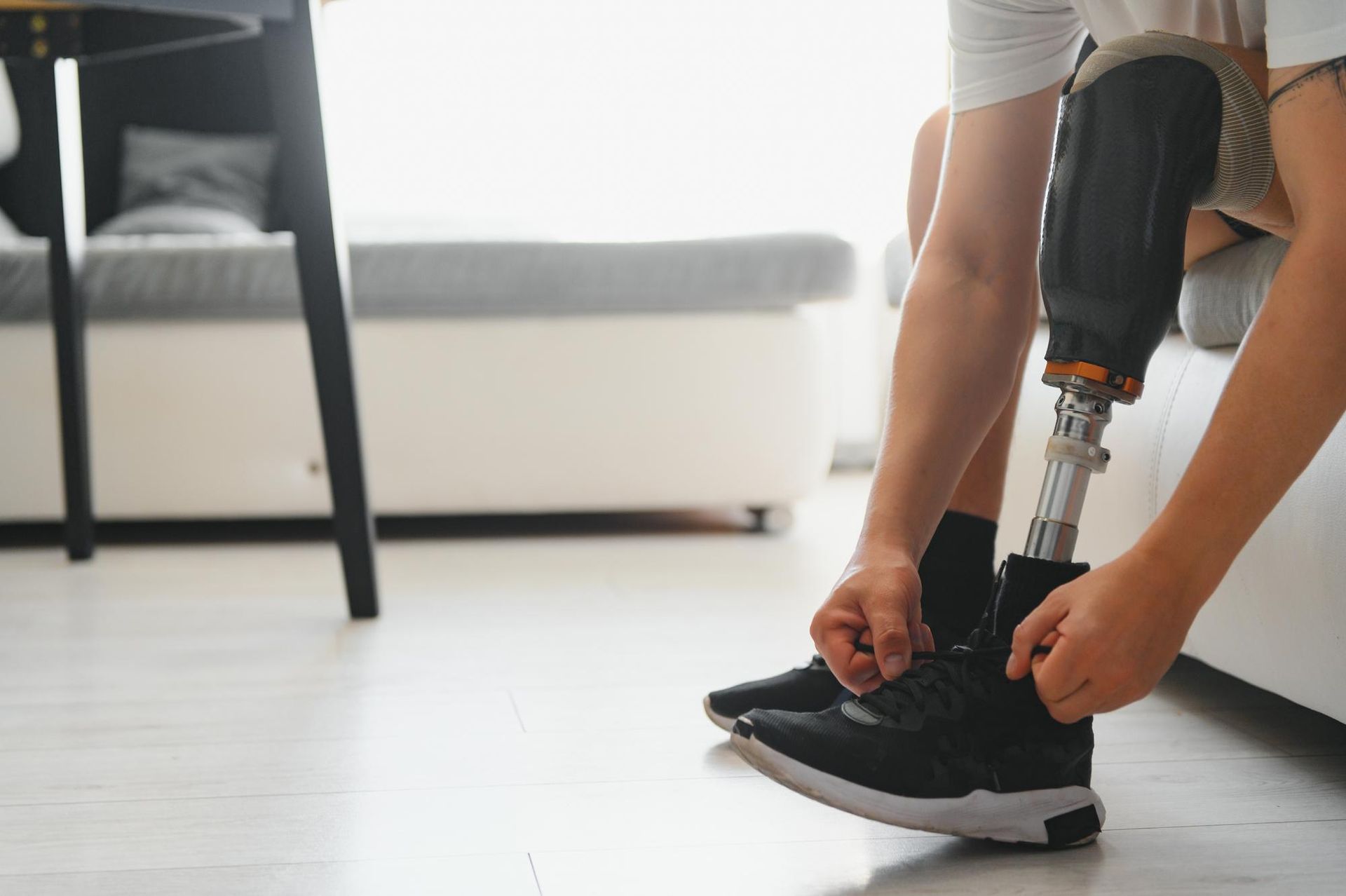 Person with a prosthetic leg ties their shoelace on a sneaker, indoors.
