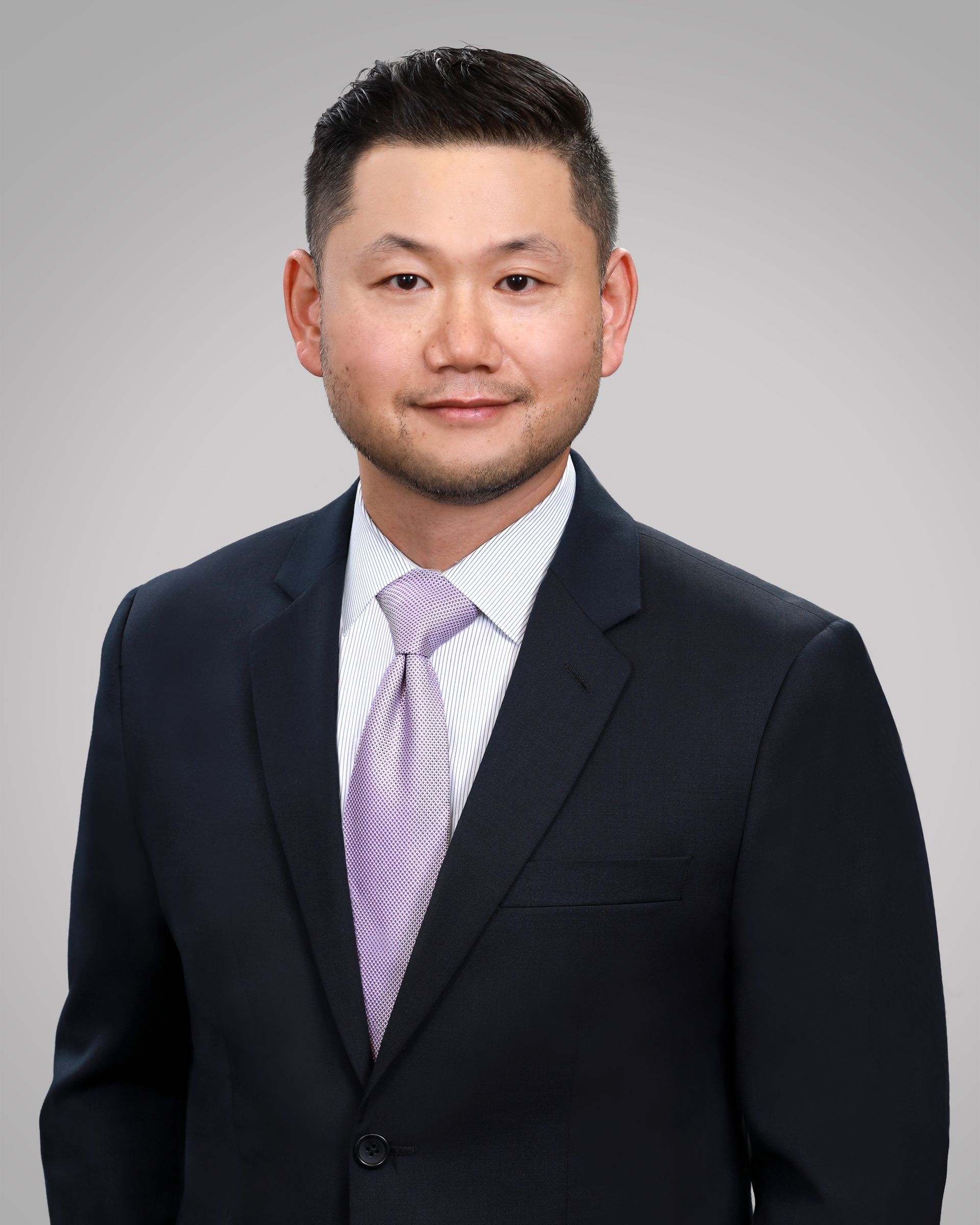 Man in suit and tie, smiling, against a gray backdrop.