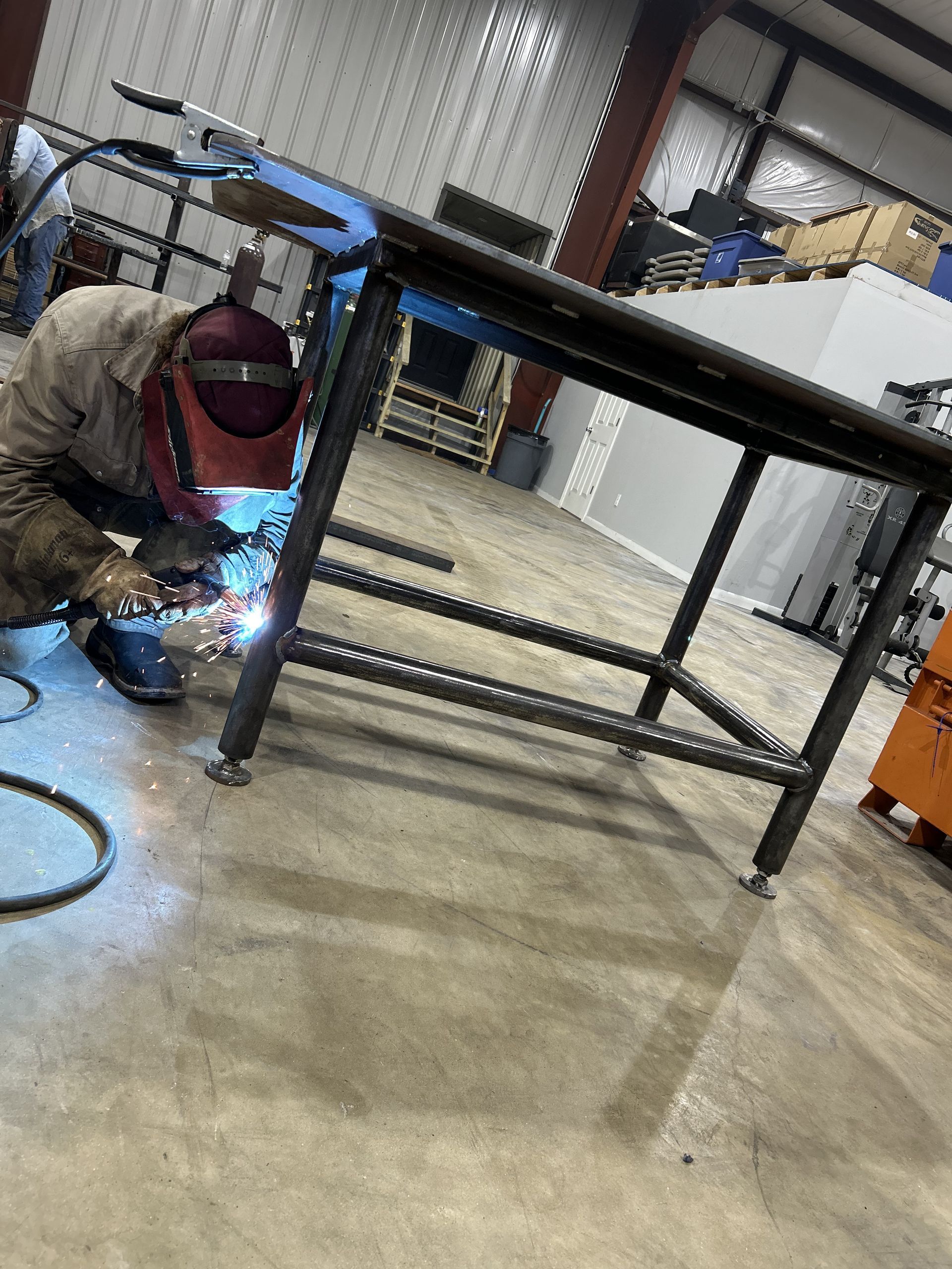 Welder in protective gear welding metal table in a workshop.
