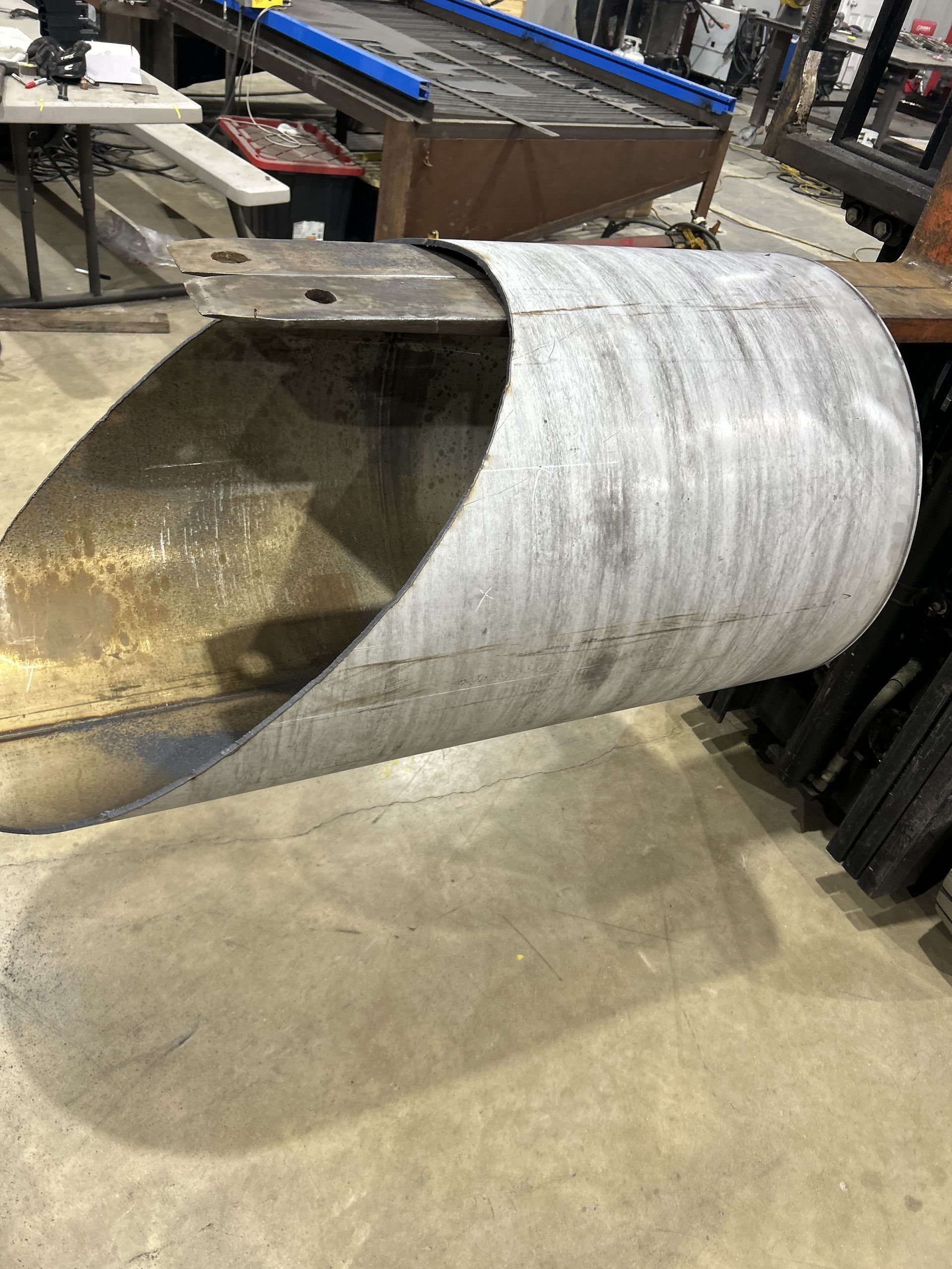 Curved metal sheet in a workshop, casting a shadow.