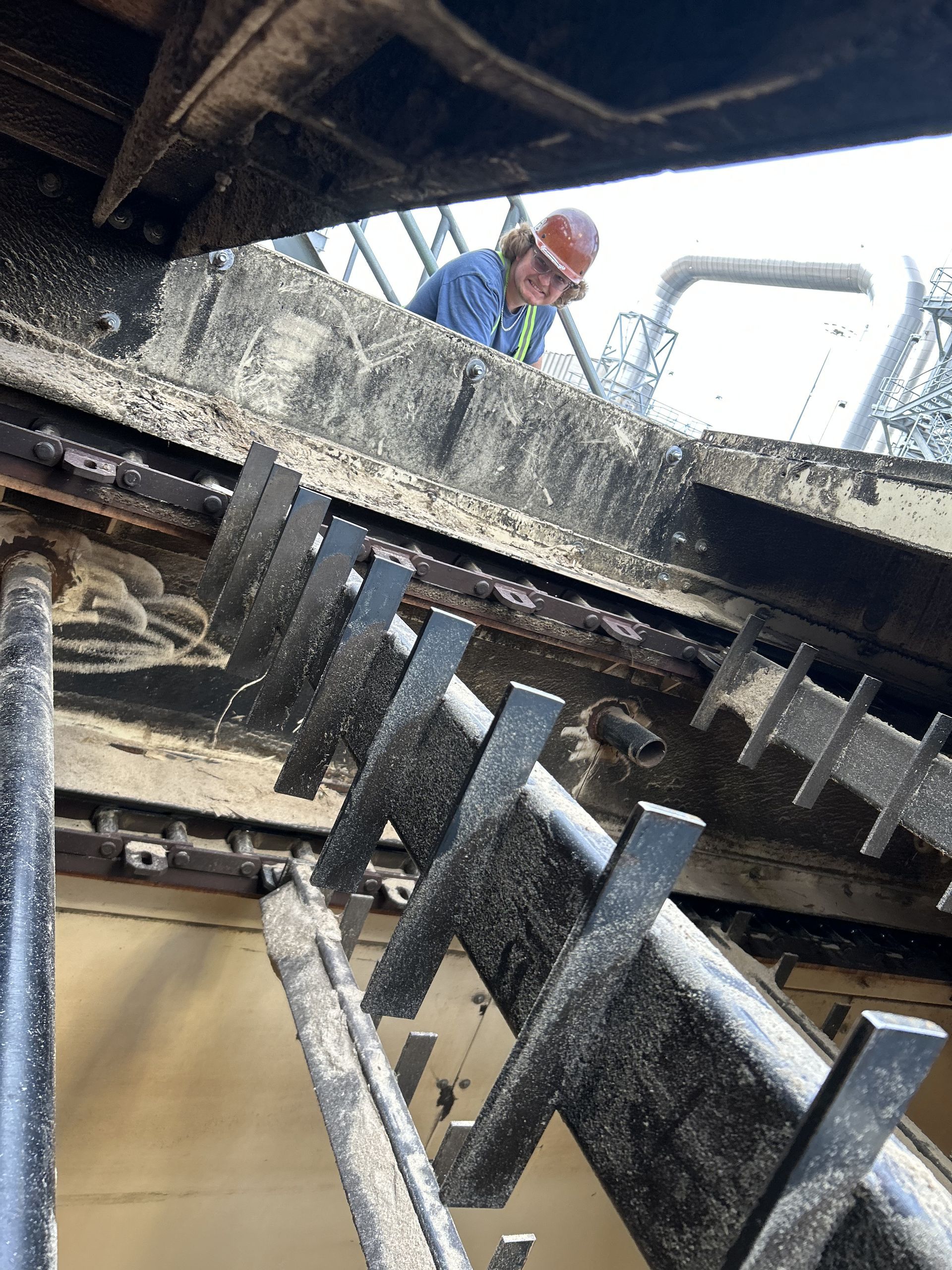 Worker in a hard hat inspecting machinery covered in white residue. Industrial setting with metal structures.