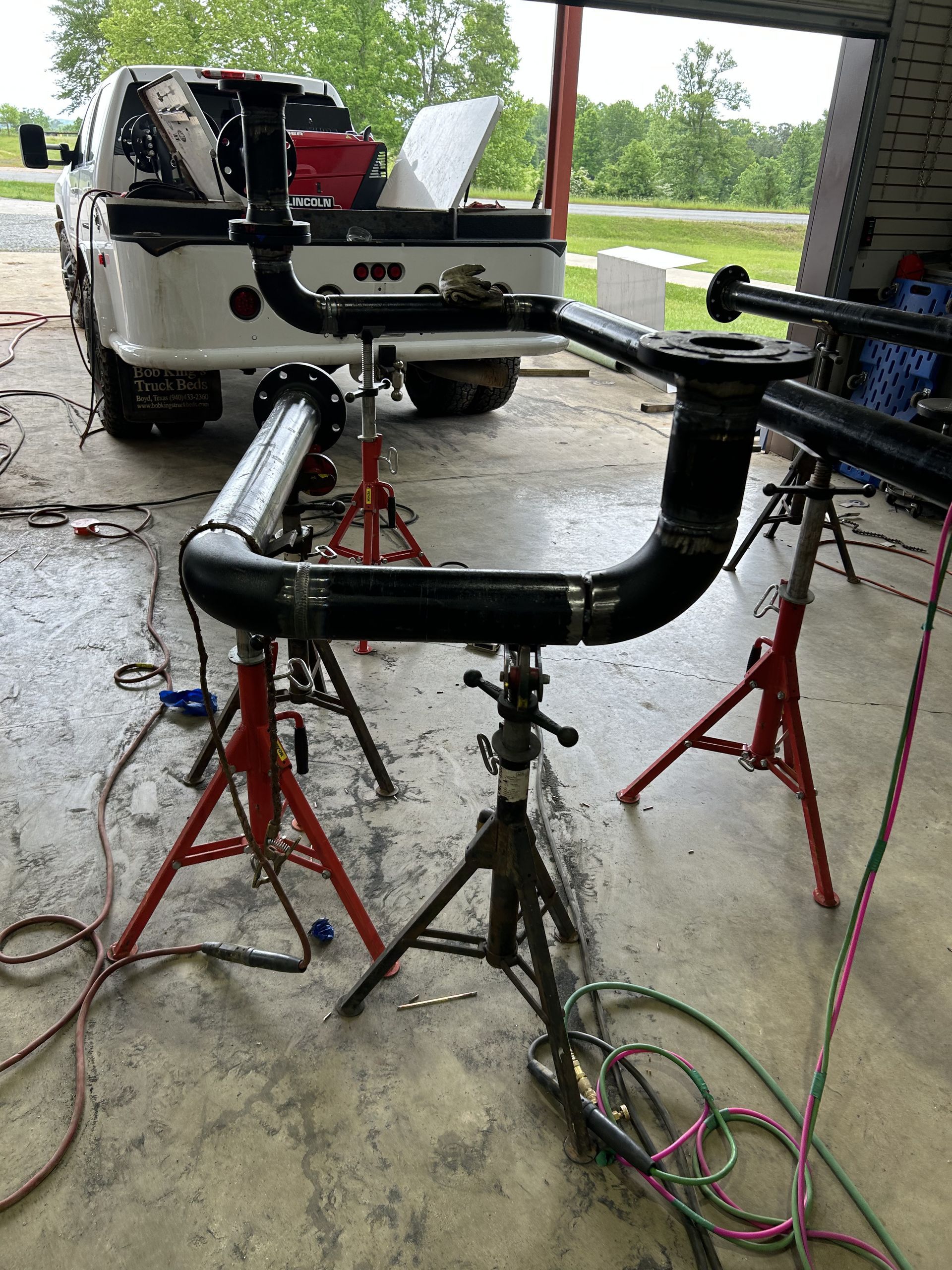 Piping system under construction; black pipes supported by red and black jack stands near a white truck.