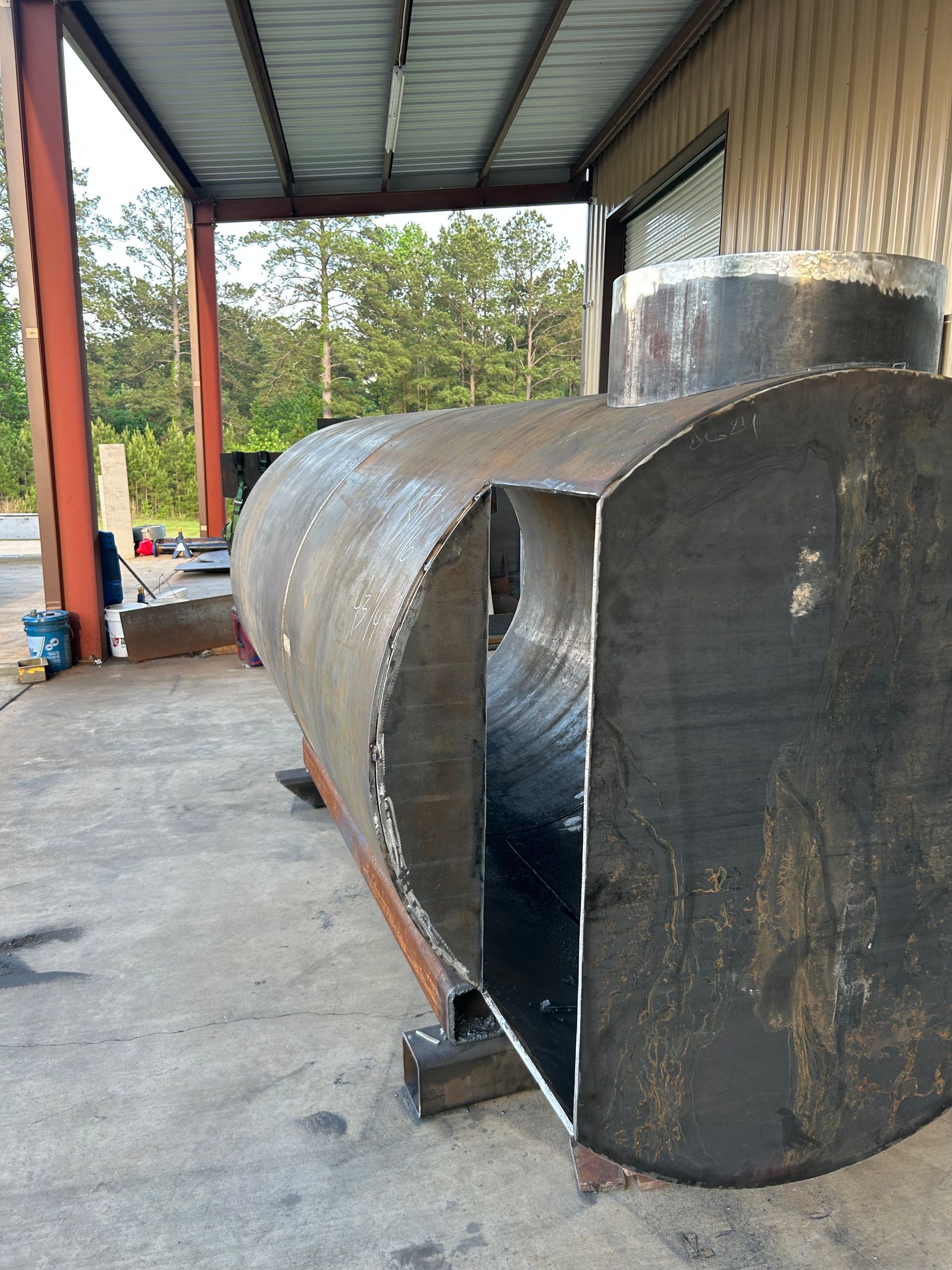 Cutaway of a large metal tank, showing interior, under a metal awning outside a building.