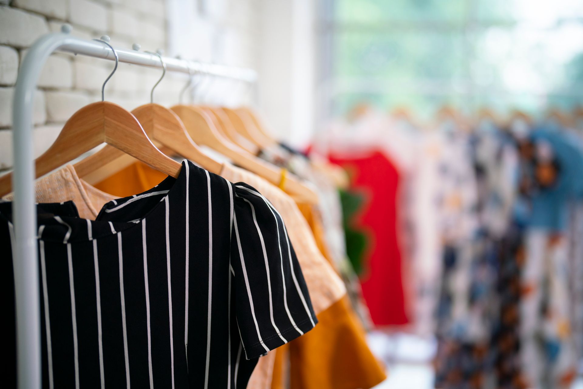 Vestiti appesi su uno scaffale all'interno di un negozio al dettaglio ben illuminato; in primo piano una camicia nera a righe.