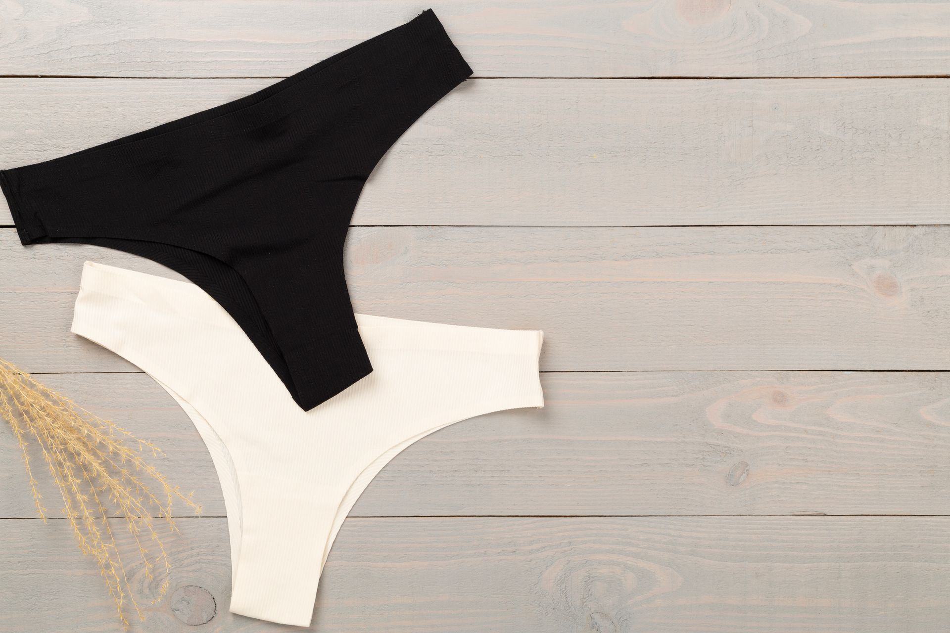 Perizoma bianco e nero su una superficie di legno grigio con steli di piante secche.