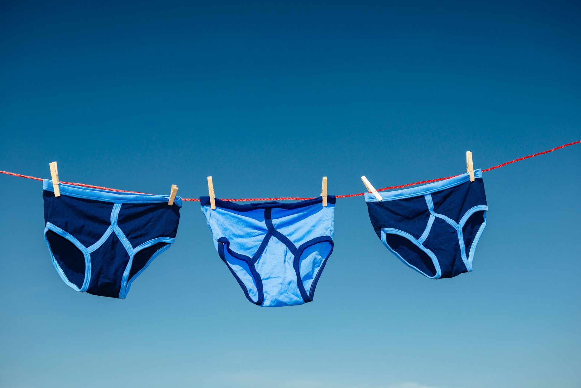 Tre paia di biancheria intima blu appese a uno stendino contro un cielo azzurro e terso.
