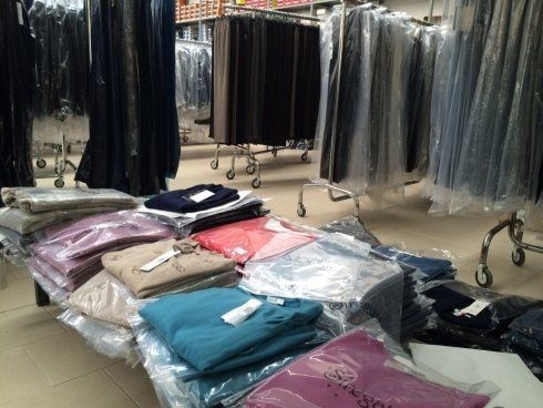 Esposizione di un negozio di abbigliamento: maglioni impilati e confezionati in vari colori; scaffali di pantaloni sullo sfondo.