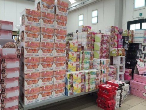 Pile di scatole assortite, probabilmente contenenti merce, in un ambiente di vendita al dettaglio. Prevalentemente scatole rosa, bianche e colorate.