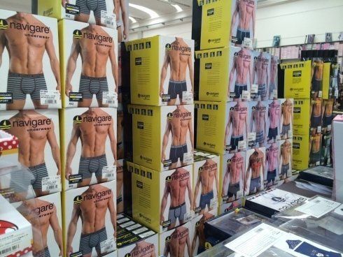 Scatole di biancheria intima maschile impilate in esposizione; modelli a torso nudo con la schiena rivolta verso la telecamera; ambientazione del negozio.