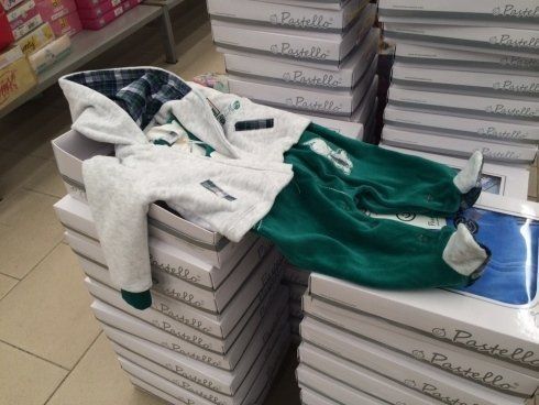 Set di vestiti per neonati, pantaloni verdi e felpa bianca con cappuccio, esposti su scatole in un negozio.