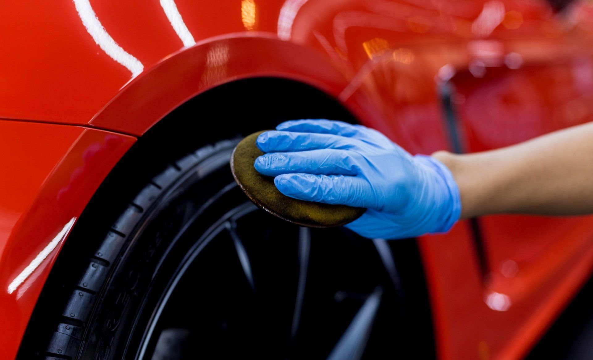 A person wearing blue gloves is polishing a red car with a sponge.