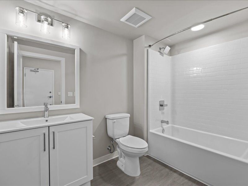 White bathroom with a vanity, toilet, and bathtub. Gray walls, white subway tile.