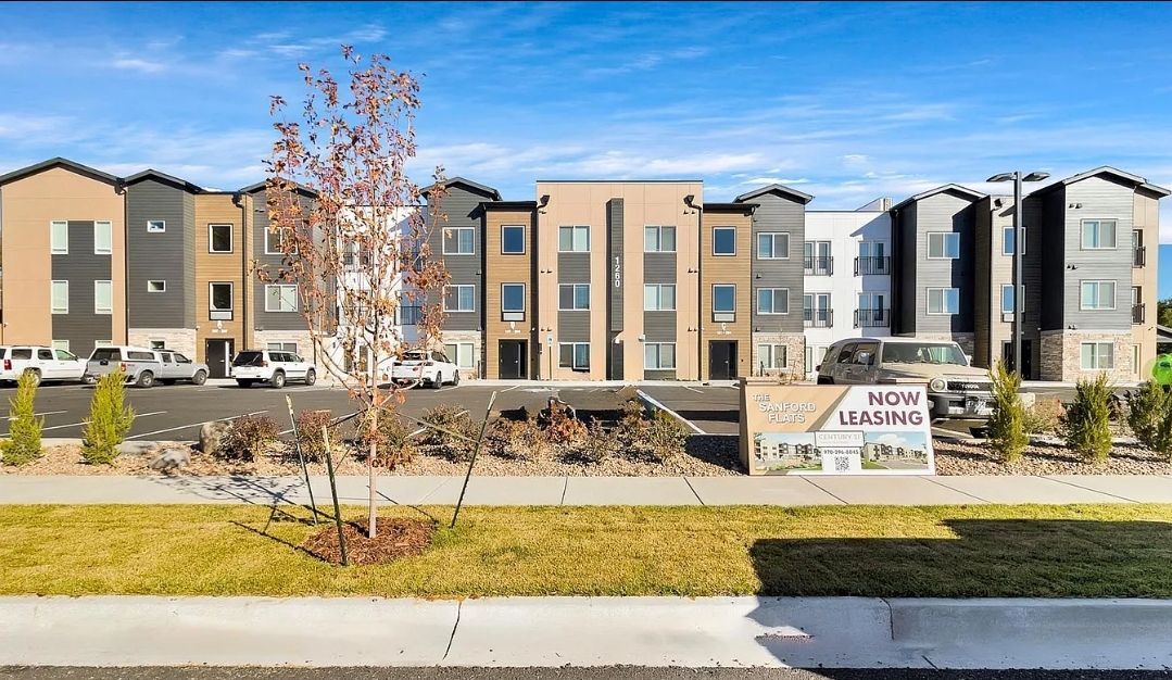 Multi-story apartment buildings with varied color schemes against a blue sky, vehicles parked on the street.