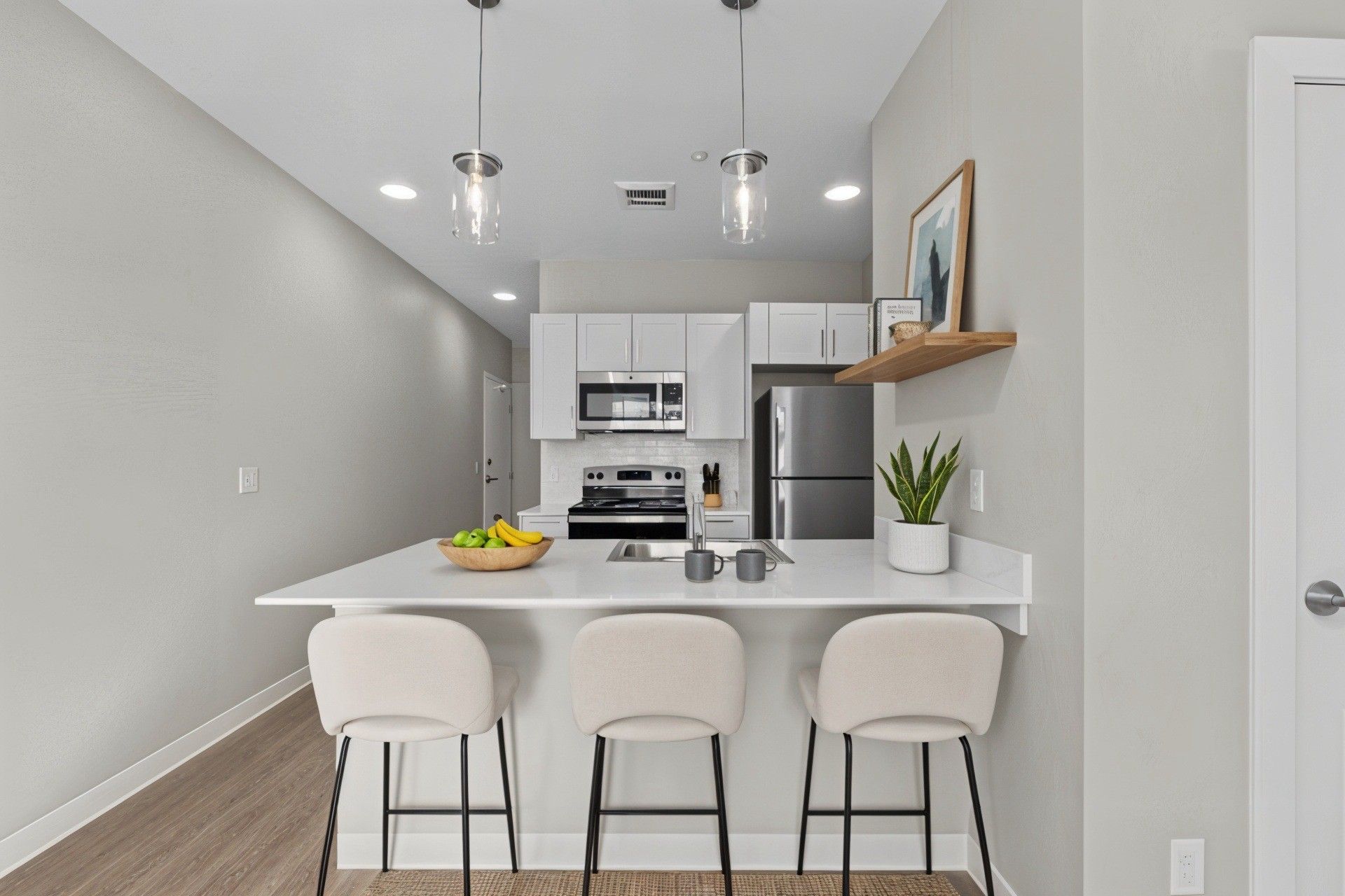 Modern kitchen with white countertops, three barstools, and stainless steel appliances.