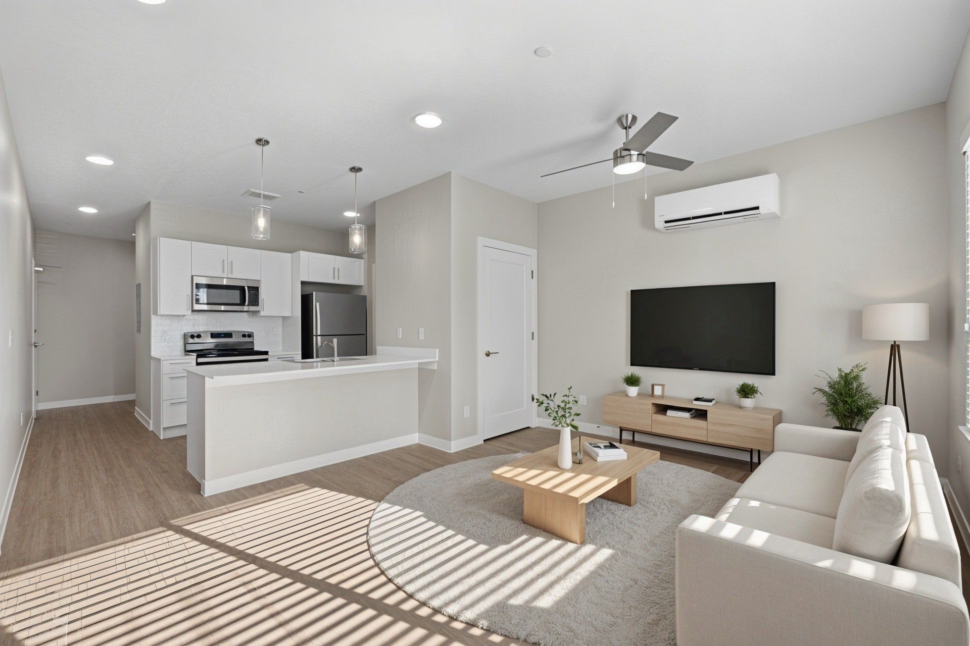 Modern living room with kitchen, a couch, TV, and light wood flooring.