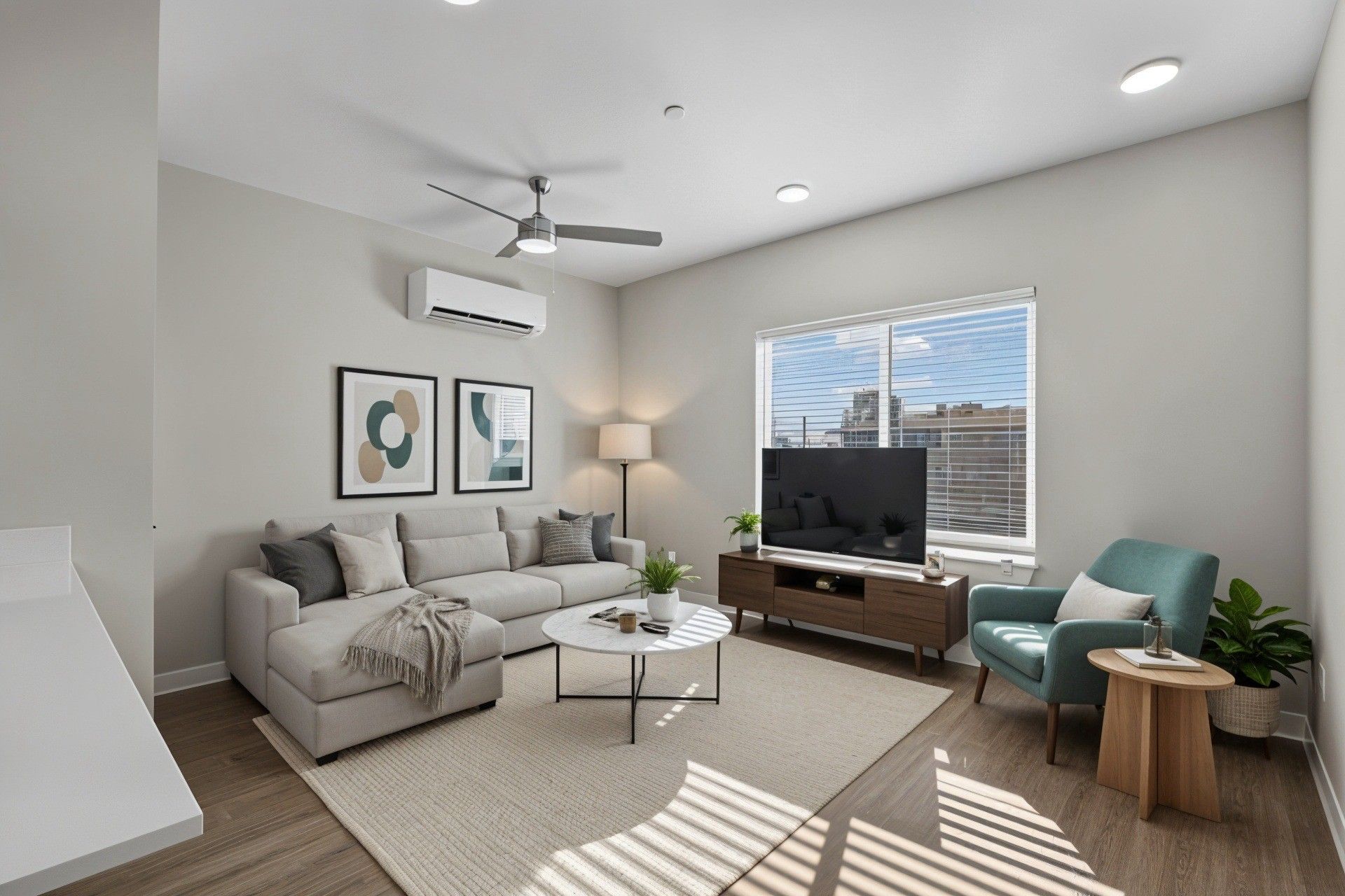 Cozy living room with a sectional sofa, TV, and armchair; light gray walls, wooden floors, and a sunny window.