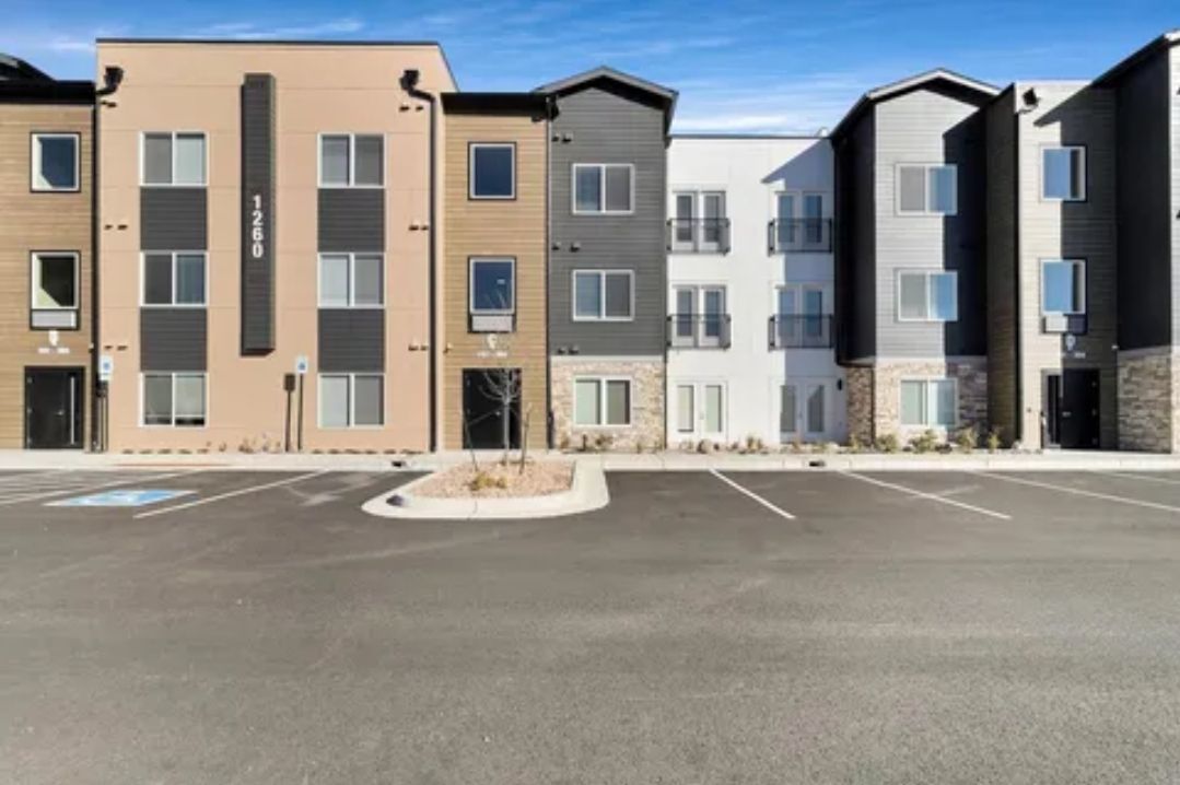 Multi-story apartment building with parking in front, under a blue sky.