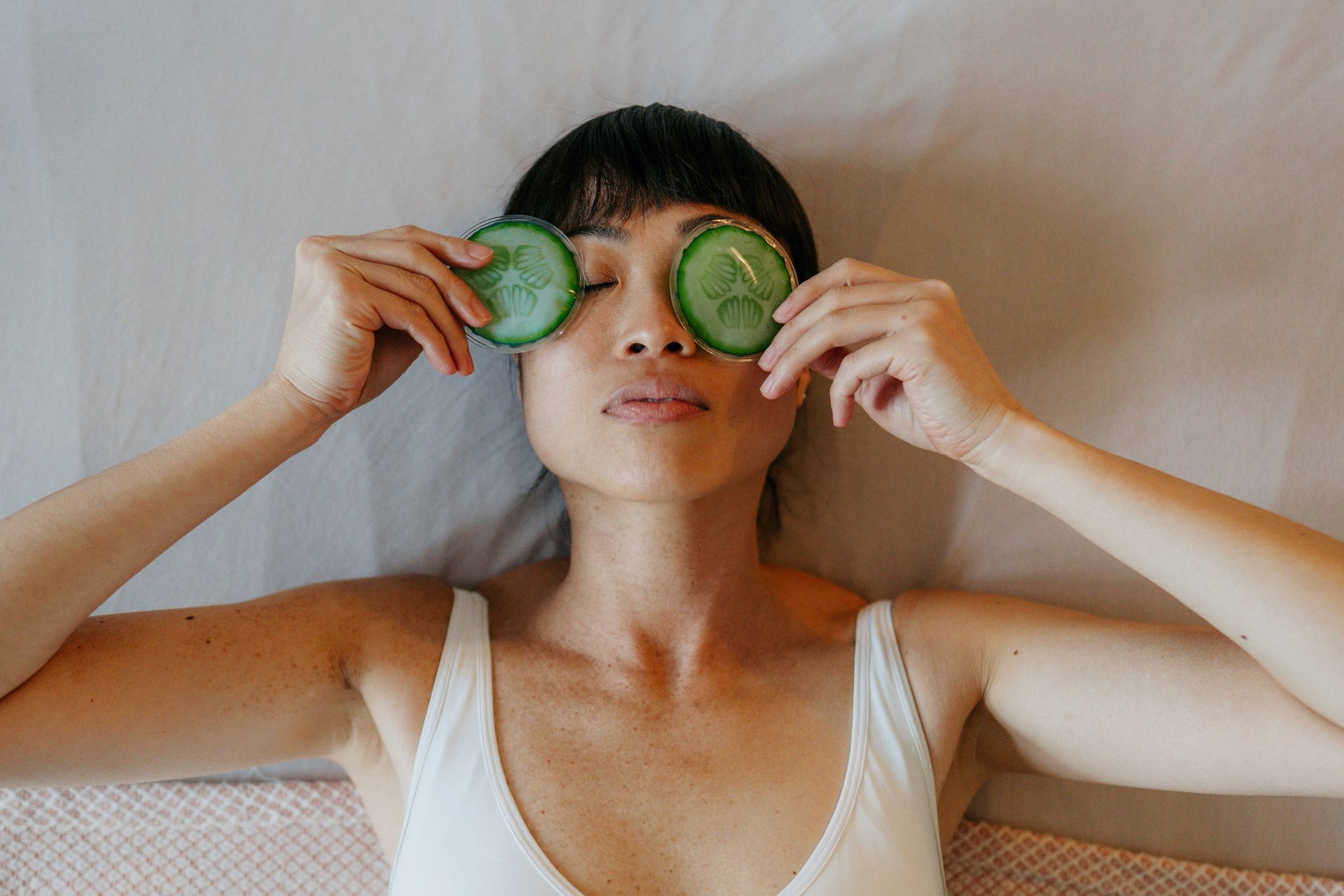A woman is laying on a bed with cucumber slices on her eyes.