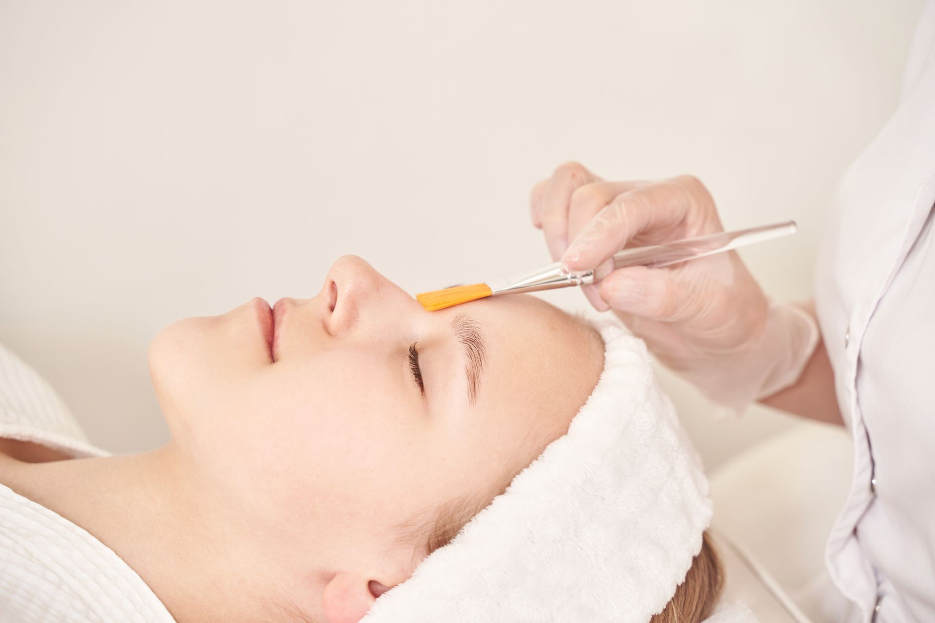 Cosmetic treatment applying product to a woman’s eyebrow with a brush and syringe-like tool