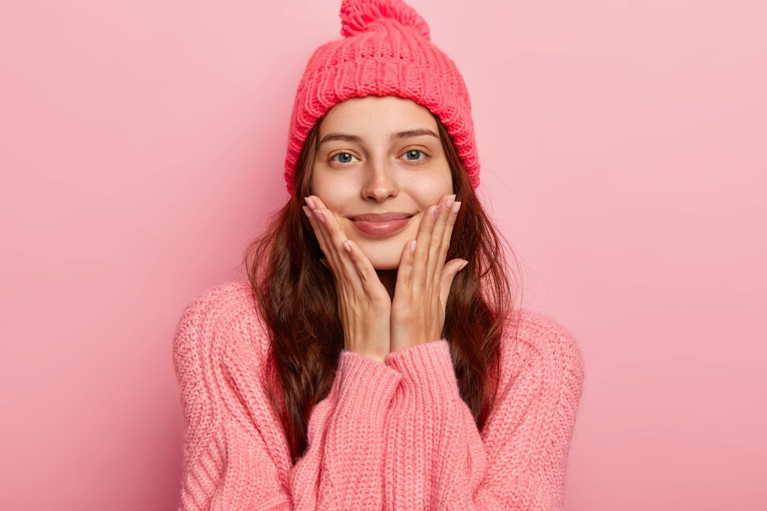 The woman is wearing a pink hat and sweater and smiling.