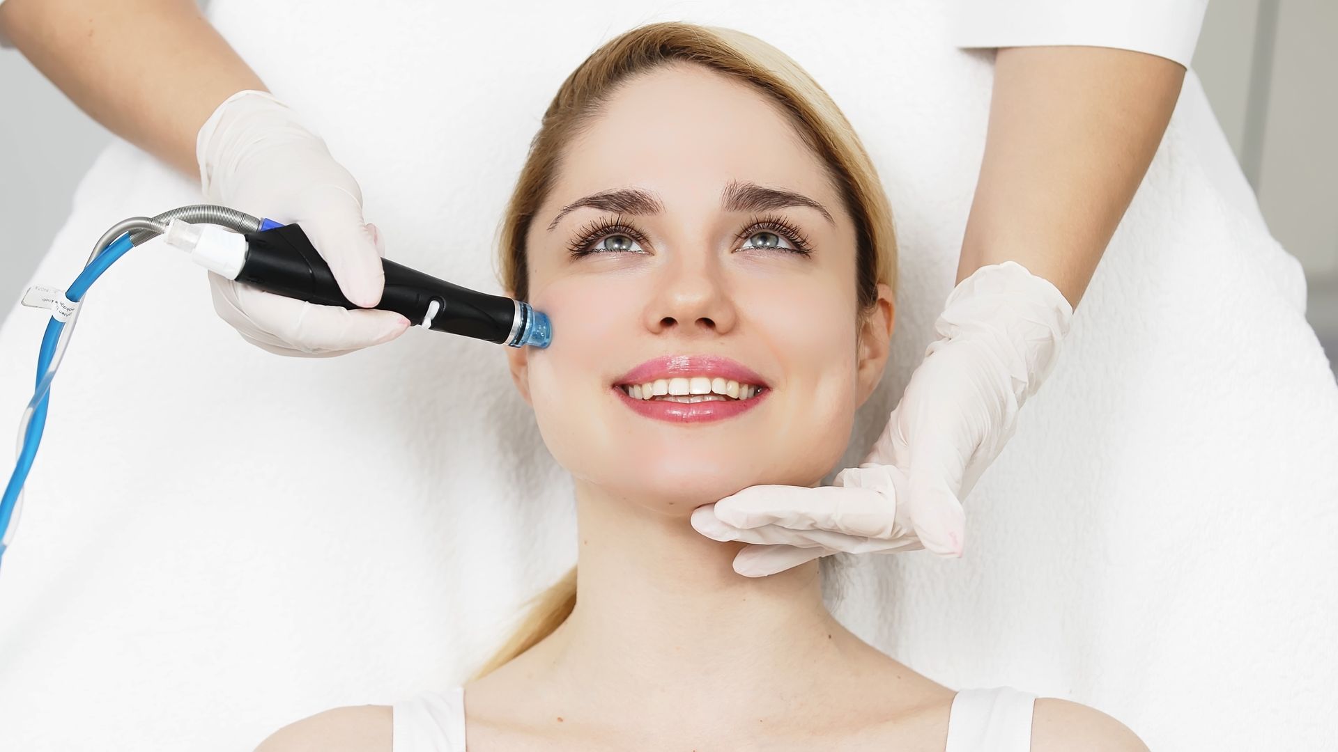 Aesthetic treatment on a smiling woman’s face with a handheld device and gloved hands