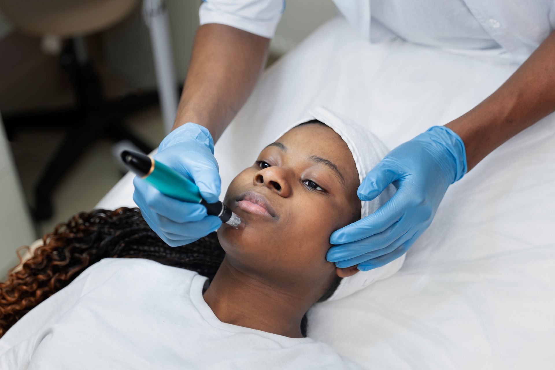 Woman receiving lip treatment. Professional with gloved hands using a device on the woman's face, lying on a white surface.