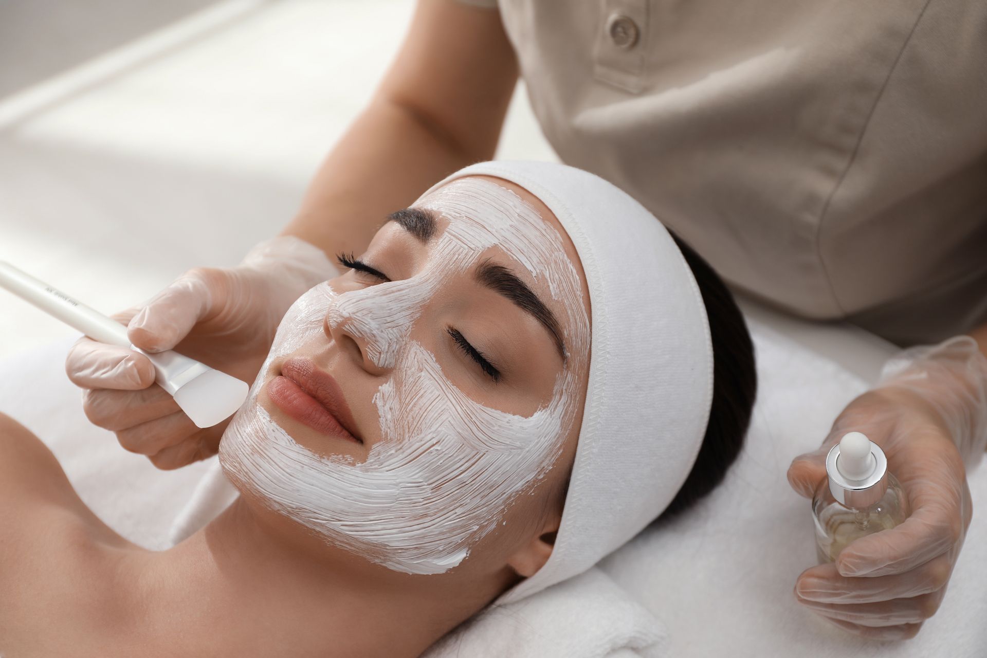 Woman receiving a facial mask applied with a brush at a spa.