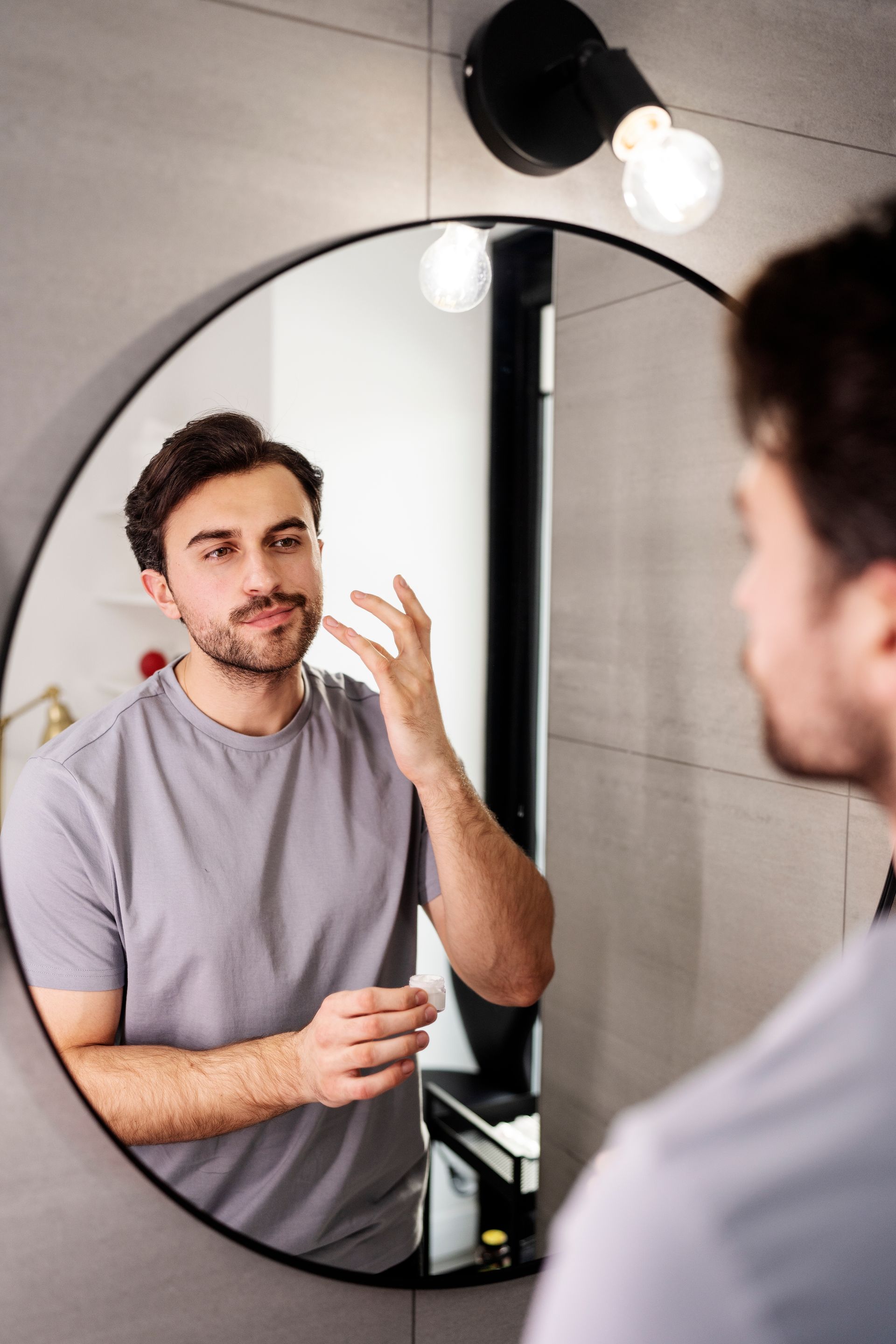 a man looking at his face in a round mirror